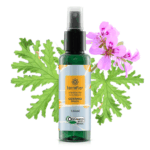 Frasco do hidrolato de gerânio brasil orgânico com a planta ao fundo.